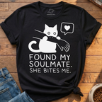 A black graphic t-shirt featuring a white cartoon cat biting a hand with the text 'FOUND MY SOULMATE. SHE BITES ME.